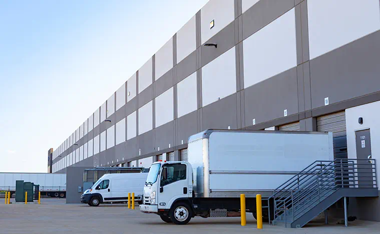Modern distribution center with docked box truck, cargo van, and loading bays. Ideal for logistics, shipping, delivery, freight, warehouse, and supply chain industry visuals for small business ads.
